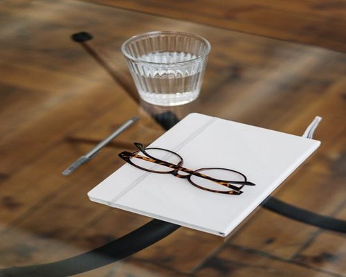 A glass of clean water standing on a wooden table next to a notebook during an office break