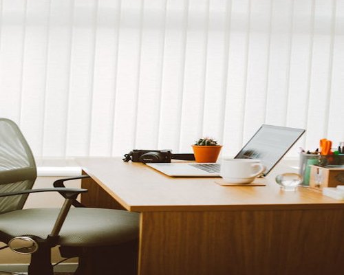A laptop computer sitting on a clean wooden desk with soft background lighting, showing a healthy workplace ergonomics environment